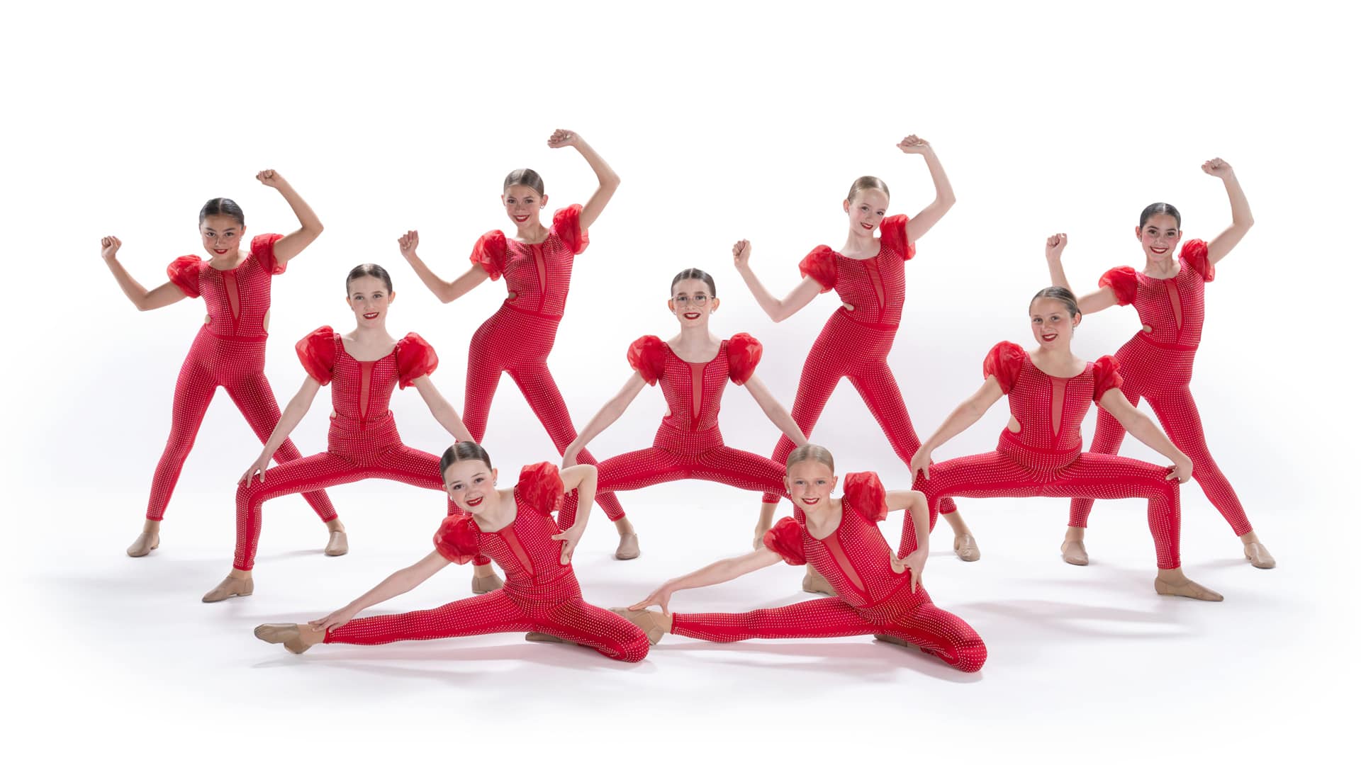 Nine children in matching red costumes pose in two rows, the front doing splits and the back row flexing their arms in a strong pose, all smiling against a white background—a playful genre shuffle of strength and flexibility.
