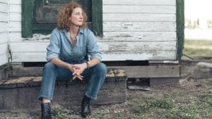 Musician Kathleen Edwards with curly red hair sits on the steps of a weathered wooden building.